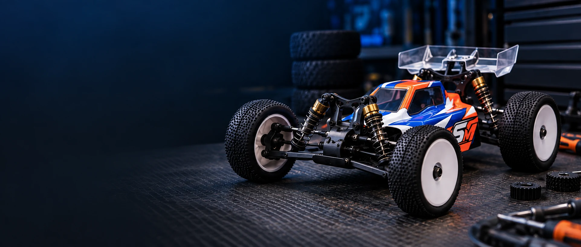 Orange, blue, and white RC buggy on a dark workshop bench.